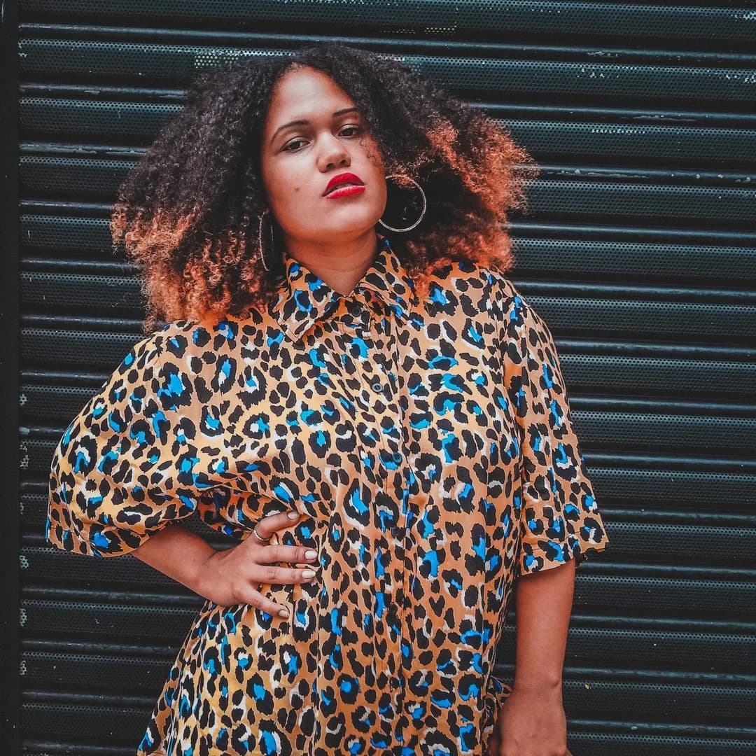 Modelo de cabelo cacheado com a camisa onça amarela de manchas pretas e azuis